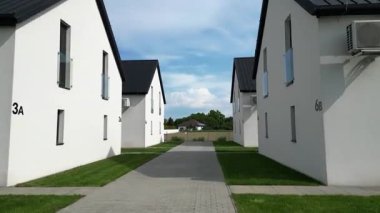 Çağdaş mimaride siyah çatıları olan iki beyaz bina, bir patikayla bağlanmış, yeşil ve açık alanlarla çevrili, açık gökyüzü altında.