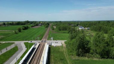 Canlı yeşil alanlar ve ağaçlarla çevrili, ufuk çizgisine uzanan raylarla manzaralı tren istasyonu manzarası sakin ve davetkar bir atmosfer yaratıyor.