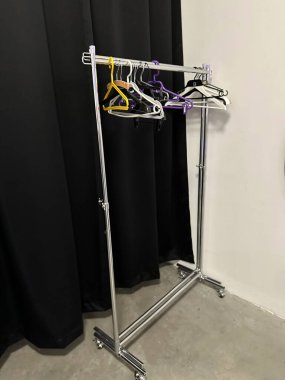 Modern giyim rafları siyah perdelere karşı dizilmiş renkli askılara sahiptir, giysi için organize bir vitrin sağlar ve moda sunumunu geliştirir.