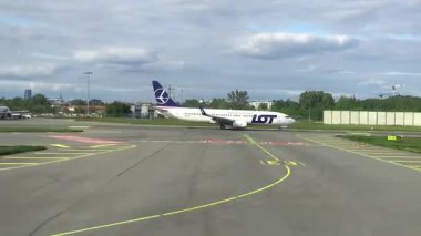 Nice, Fransa - 13 Mayıs 2025: Uçak, yeşil çimen ve şehrin ufuk çizgisi ile dinamik havaalanı çevresini yakalamak üzere terminale doğru pist üzerinde ilerliyor.