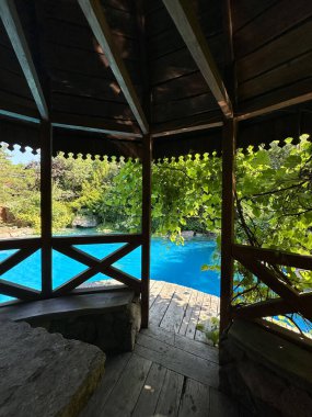 Parlak yeşilliğe sahip ahşap çardak, huzurlu bir mavi yüzme havuzu manzarası sunuyor, dinlenmek ve keyif almak için sakin bir atmosfer yaratıyor.