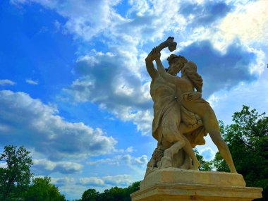 Tutkulu bir kucaklaşmada iki figürü tasvir eden sanatsal heykel, bulutlarla dolu canlı bir gökyüzüne karşı kurulmuş, bir güzellik ve bağlantı anını yakalıyor.