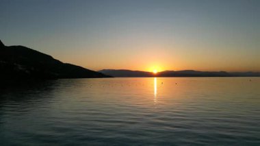 Tranquil sunset unfolds over still waters, with soft waves mirroring warm hues, creating a peaceful atmosphere in a stunning coastal landscape