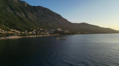 Sahil manzarası, sakin sular üzerinde akşam ışığının kademeli geçişini yakalıyor, sakin bir atmosferde kıyı şeridini ve uzak dağları vurguluyor.