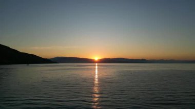 Durgun suların üzerinde büyüleyici bir güneş doğuyor, denizi yansıtan altın ışıkla, dingin ortamı güçlendiriyor ve huzur ve güzellik hissi uyandırıyor.