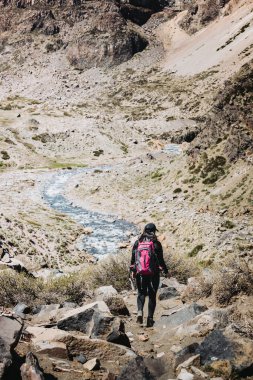 Büyük bir şelaleye giden kayalık bir yolda yürüyen kadın sırt çantalı. Yüksek kalite fotoğraf