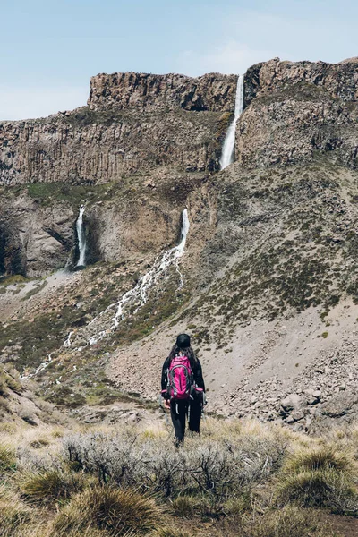 Büyük bir şelaleye giden kayalık bir yolda yürüyen kadın sırt çantalı. Yüksek kalite fotoğraf