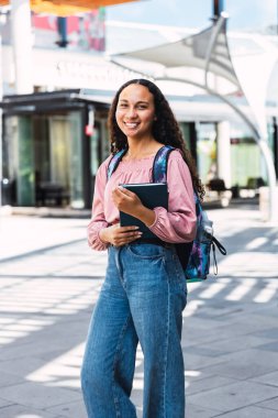Gülümseyen Latin üniversiteli kadın elinde kitaplarıyla kampüsün dışında. Yüksek kalite fotoğraf