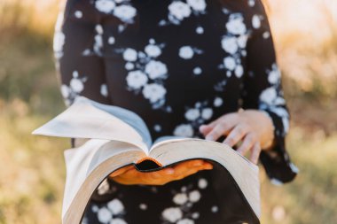 Unrecognizable young woman holding and reading her bible, outside with sun backlight. Spiritual revival. High quality photo