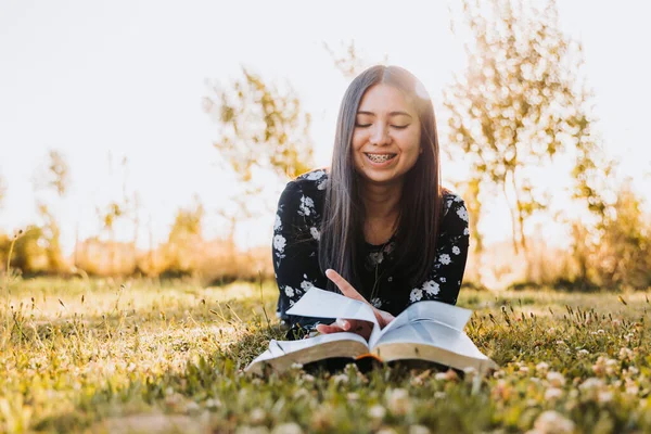 Young believing girl lying on the grass and studying her bible, in the field at sunset. Copy space. High quality photo