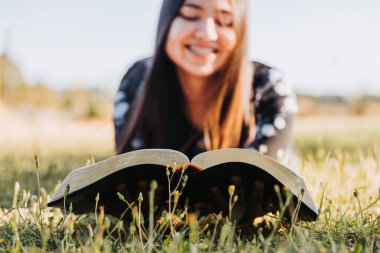 Close up of a young woman lying while reading the bible on the grass with a blurred background. High quality photo