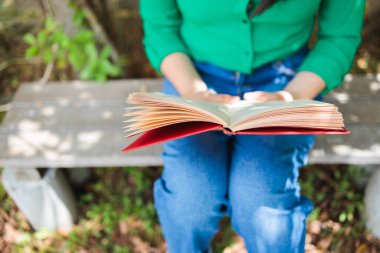 Unrecognizable student girl reading a book in the backyard. World Book Day. Benefits of reading. High quality photo