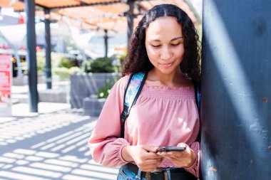 Latin university student woman smiling and using her mobile outside the mall in her free time. High quality photo