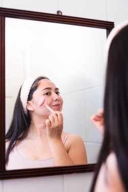 Yanağında gül kuvars yüz silindiri kullanan genç bir kadın. Güzel cilt bakımı. Yüksek kalite fotoğraf