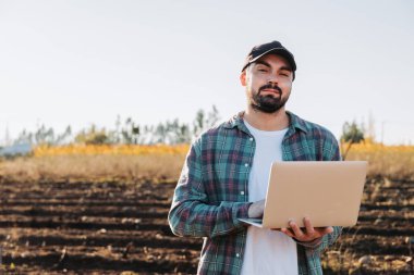 Genç latin çiftçi tarlasının ortasında dizüstü bilgisayarıyla telgraf çekiyor. Tarım sürdürülebilirliği. Yüksek kalite fotoğraf