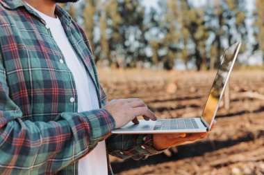 Genç latin çiftçi tarlasının ortasında dizüstü bilgisayarıyla telgraf çekiyor. Tarım sürdürülebilirliği. Yüksek kalite fotoğraf