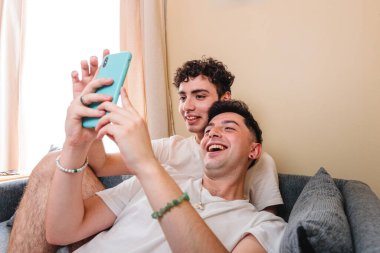 Young smiling gay couple using the smart phone to watch entertaining content. LGBT people routine. High quality photo