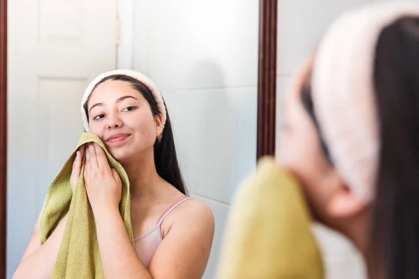 Young woman on the mirror, wiping her face with a green towel. Skin care at home. High quality photo