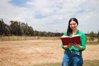 Smiling old fashioned young woman reading a book in the greenery of the field. High quality photo