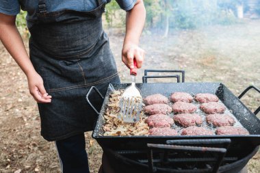 Mangal ızgarasında hamburger ve soğan hazırlayan tanınmamış Latin genç adam. Yüksek kalite fotoğraf