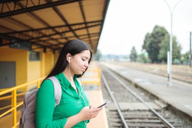 Bir tren istasyonunda, akıllı telefonuyla sosyal medyada gezinen Latin bir genç kadının yan görüntüsü. Yüksek kalite fotoğraf