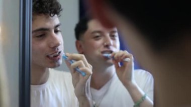 Homoseksüel çift dişlerini fırçalıyor ve aynaya bakıyor. Eşcinsel bir çiftin günlük hayatı. 4k video