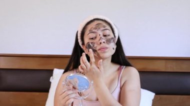 Genç bir kadın yatağında, nemlendirici yüz maskesi takıyor. Evde cilt bakımı. 4K video