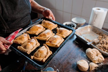 Geleneksel Şili Mutfağı: Rustik Mutfağında Bir Tepsi Fırınlanmış Empanadas Tutan Tanınmayan Latin Kadın. Yüksek kalite fotoğraf