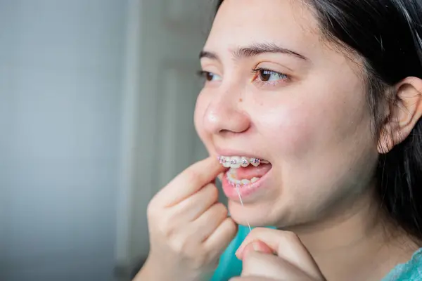 Close up of young woman with braces using dental floss to clean her teeth in the bathroom. Oral Hygiene routine. High quality photo