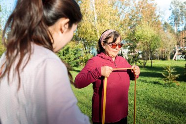 İspanyol kıdemli kadın, çimlerin üzerinde antrenör tarafından rehberlik edilen direnç bantlarıyla egzersiz ve fitness aktivitesi yapıyor. Yüksek kalite fotoğraf