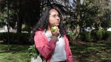 Eko-Dost: Genç Latin Kadın Erdemli Park Yürüyüşü sırasında Taze Yeşil Elmanın Tadını Çıkarıyor. Sürdürülebilir ve sağlıklı bir hayat. Yüksek kalite 4k görüntü