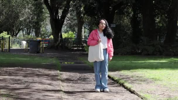 持続可能なライフスタイル グリーンプラクティスを推進するラテン女性 農場フレッシュプロデュースの再利用可能なバッグで公園を歩きます 高品質の4K映像 — ストック動画