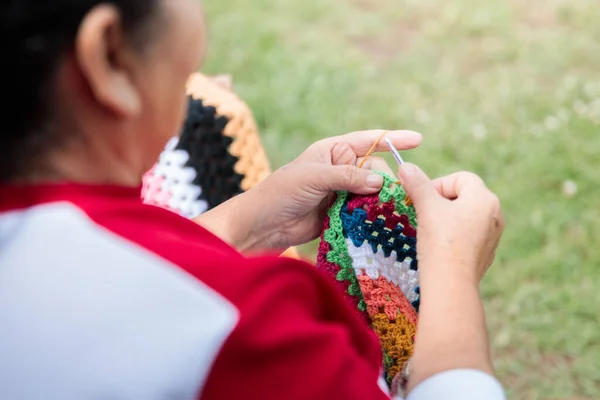 Elderly Senior latin woman with crafts skills knitting a colorful blanket in the garden of her country house. Rear view. High quality photo