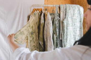 Üzerinde doğal çiçek boyası olan bir gömlek tutan bir tekstil sanatçısının dikiz görüntüsü. Lifli kıyafet dolabında botanik parmak izi. Yüksek kalite fotoğraf