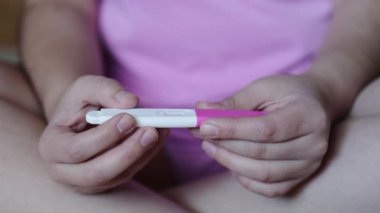 Tanımlanamayan endişeli genç kadın, pembe pijamalı, yatağında hamilelik testi sonuçlarını görüyor. Yüksek kalite 4k görüntü