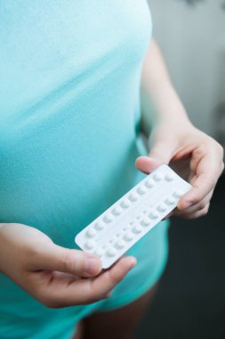 Tanınmayan genç bir kadın, turkuaz pijama giyiyor, doğum kontrol haplarını banyoda dururken tutuyor. Yüksek kalite fotoğraf