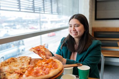 Gülümseyen genç Latin kadın restoranda bir dilim pepperoni pizza yiyor. Bir arkadaşıyla yemeğin tadını çıkarıyor. Yüksek kalite fotoğraf