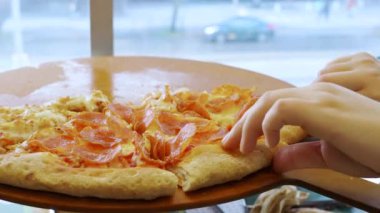 Kamera arkası hareketinde Latin bir kadın restoranda bir dilim pepperoni pizza yiyor. Bir arkadaşıyla yemeğin tadını çıkarıyor. 4k video