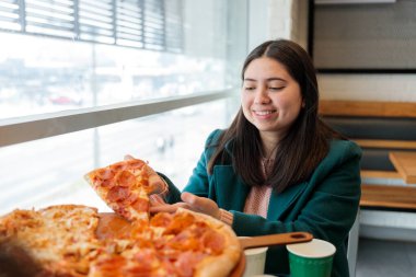 Gülümseyen genç Latin kadın restoranda bir dilim pepperoni pizza yiyor. Bir arkadaşıyla yemeğin tadını çıkarıyor. Yüksek kalite fotoğraf