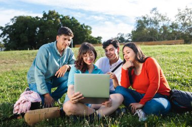 Bir grup öğrenci bilgisayar kullanıyor, dışarıda öğrenme ve parkta işbirliği yapmayı seviyorlar.