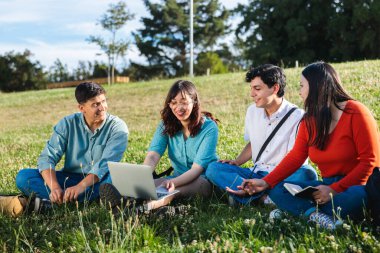 Bir grup mutlu Latin sınıf arkadaşı dersten sonra parkta oturmaktan keyif alıyor, öğleden sonra şık ve renkli kıyafetler giyiyorlar.