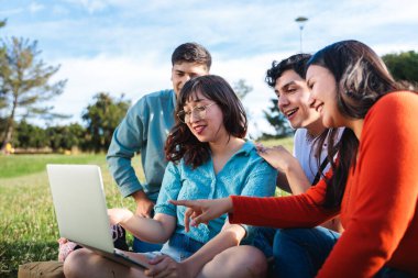 Güneşli bir parkta birlikte oturan çeşitli öğrencilerden oluşan bir grup, açık havada iş birliği yapmak için bir dizüstü bilgisayar kullanıyorlar. Okul konseptine dönelim..