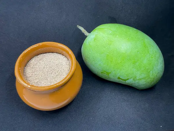 Küçük bir kavanoz, yeşil mango ve amchur tozu. Ayrıca amchur ya da mango tozu olarak da bilinir, kurutulmamış yeşil mangolardan yapılır, ekşi tat, Hint mutfağında yaygın olarak kullanılır.. 