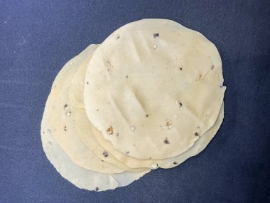 Çiğ, ince, mercimek unundan yapılmış ve karabiberle tatlandırılmış papad. Hint atıştırmalıkları siyah arkaplan 