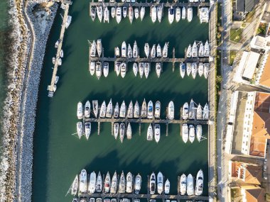 Yatı demirli ve yelkenli tekneleri olan bir marinanın havadan görüntüsü.