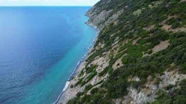 Açık mavi denize bakan sarp yeşil bir tepenin havadan görünüşü