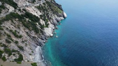 Dolambaçlı bir yolu olan kayalık bir kıyı şeridinin havadan görünüşü ve açık deniz mavisi