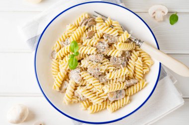 Fusilli pasta with mushrooms, cheese and fresh basil in a plate on a white wooden background