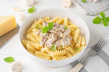 Fusilli pasta with mushrooms, cheese and fresh basil in a plate on a white wooden background