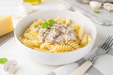 Fusilli pasta with mushrooms, cheese and fresh basil in a plate on a white wooden background
